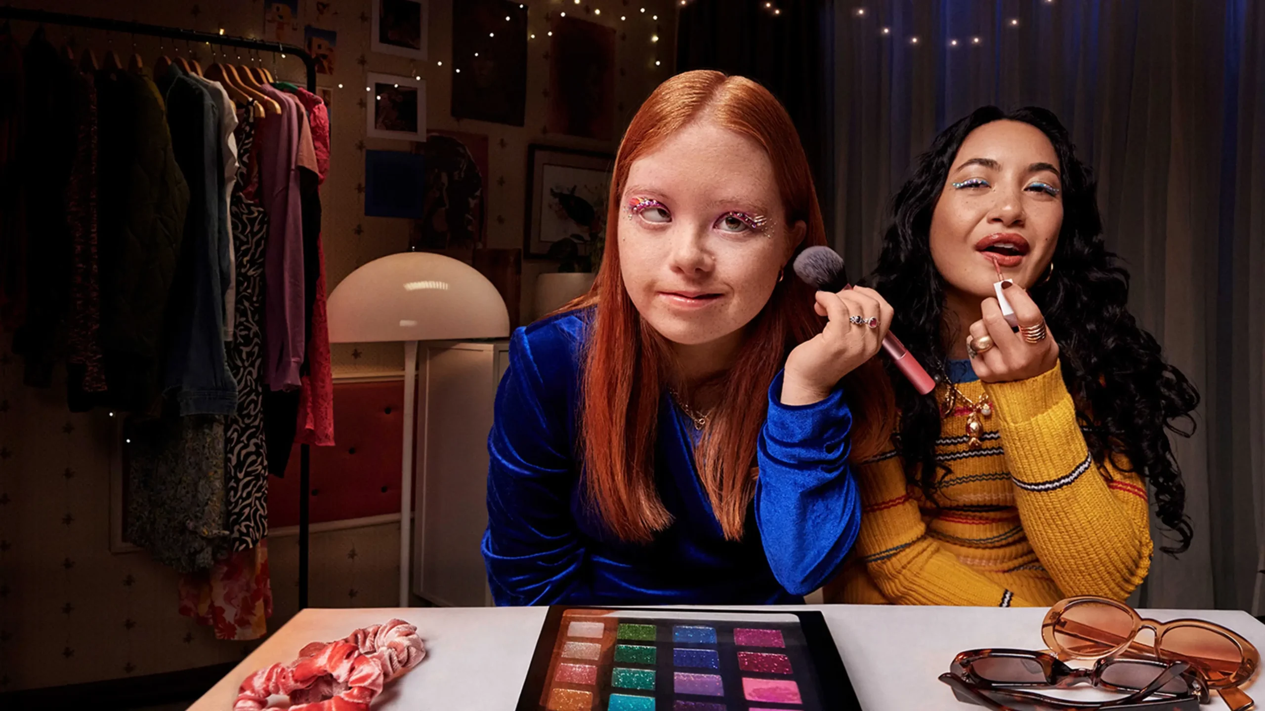 A young person and a disability support worker are looking at themselves in the mirror and smiling while applying make-up.