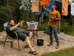 Support worker hangs washing on Hills Hoist clothesline while their client with disability talks.
