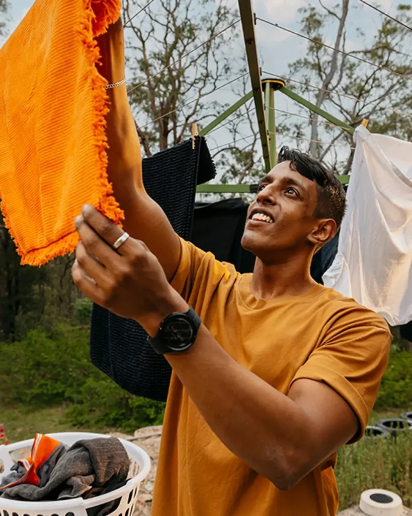 Support worker hangs an orange towel on the Hills Hoist clothesline in the backyard.