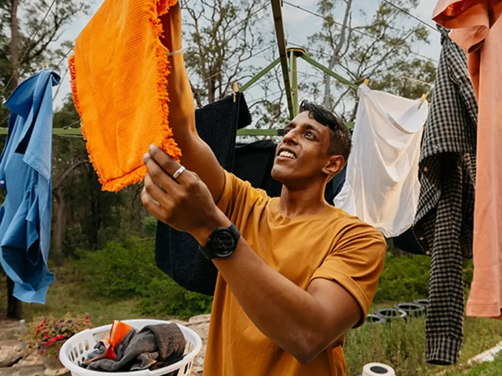 Support worker hangs an orange towel on the Hills Hoist clothesline in the backyard.