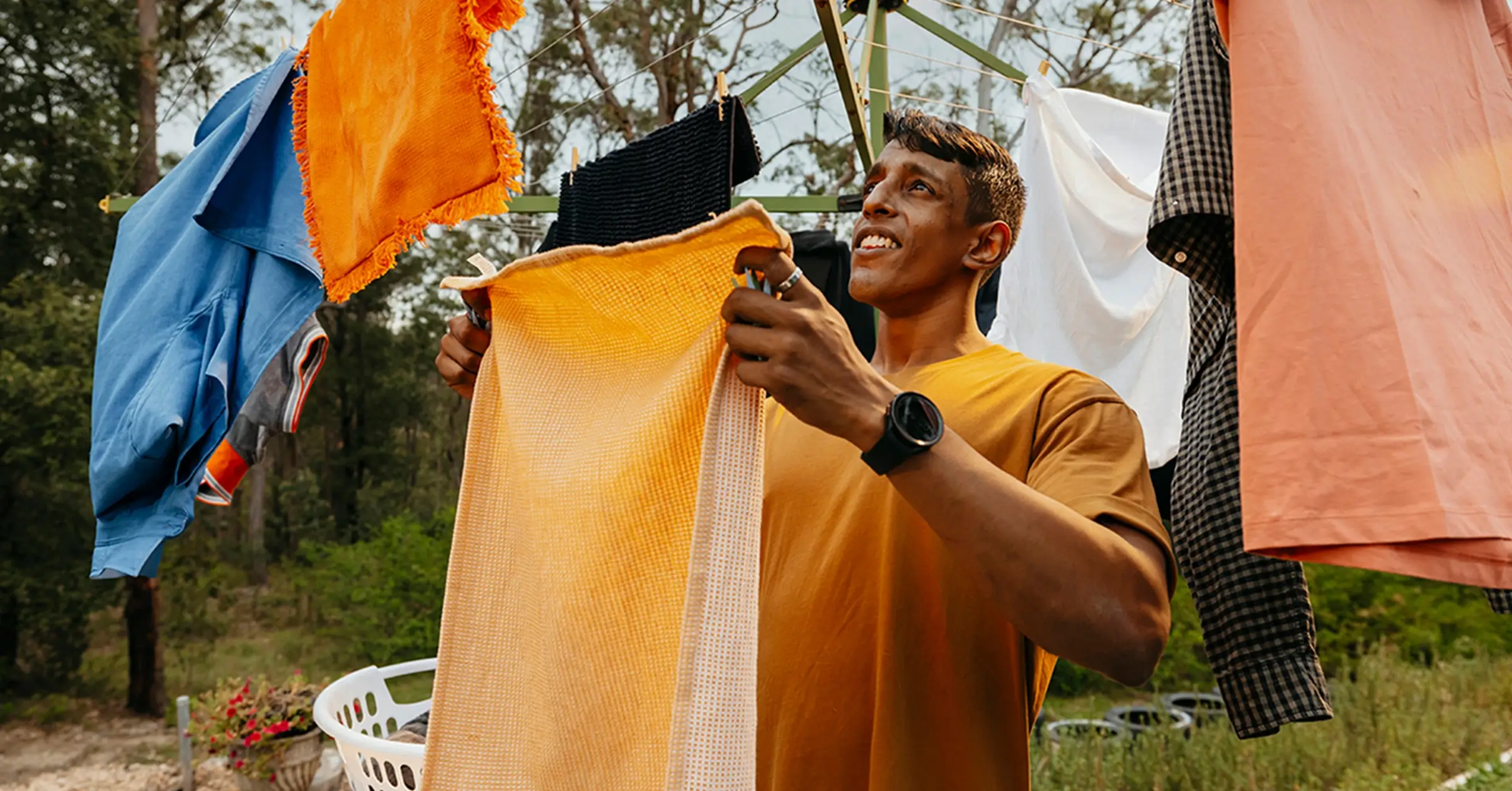 Support worker hangs an orange towel on the Hills Hoist clothesline in the backyard.
