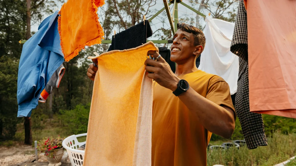 Support worker hangs an orange towel on the Hills Hoist clothesline in the backyard.