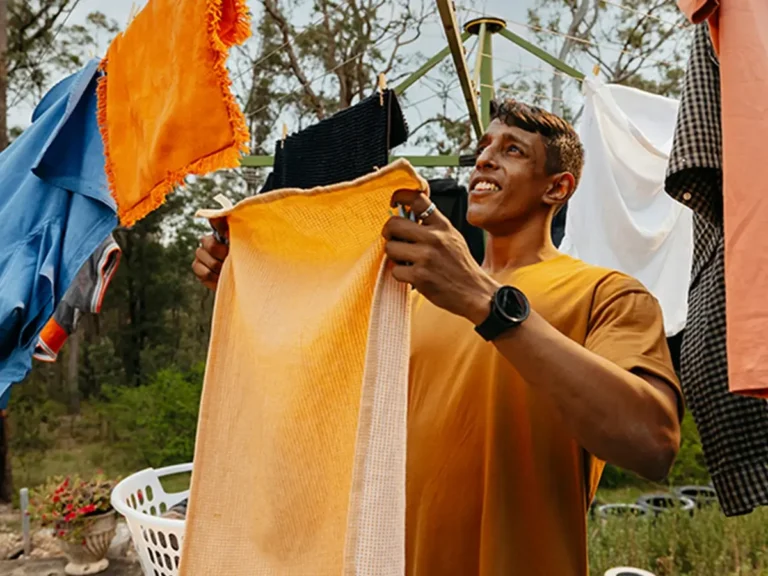 Support worker hangs an orange towel on the Hills Hoist clothesline in the backyard.