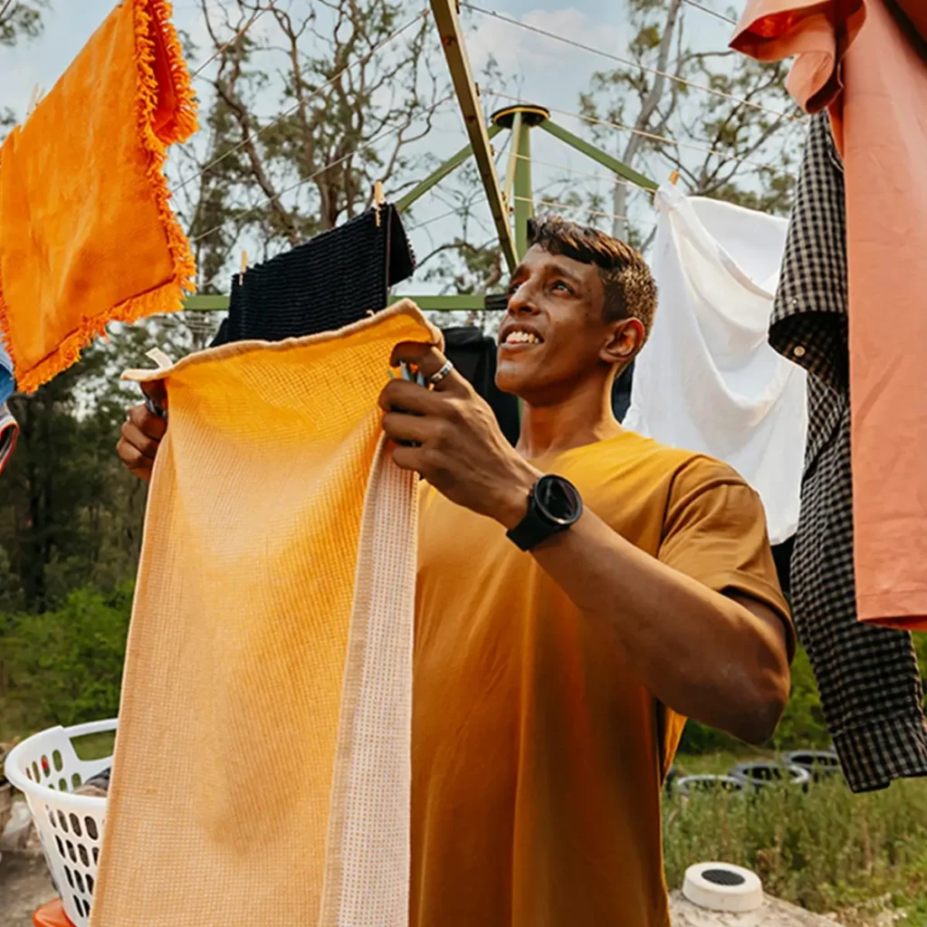 Support worker hangs an orange towel on the Hills Hoist clothesline in the backyard.