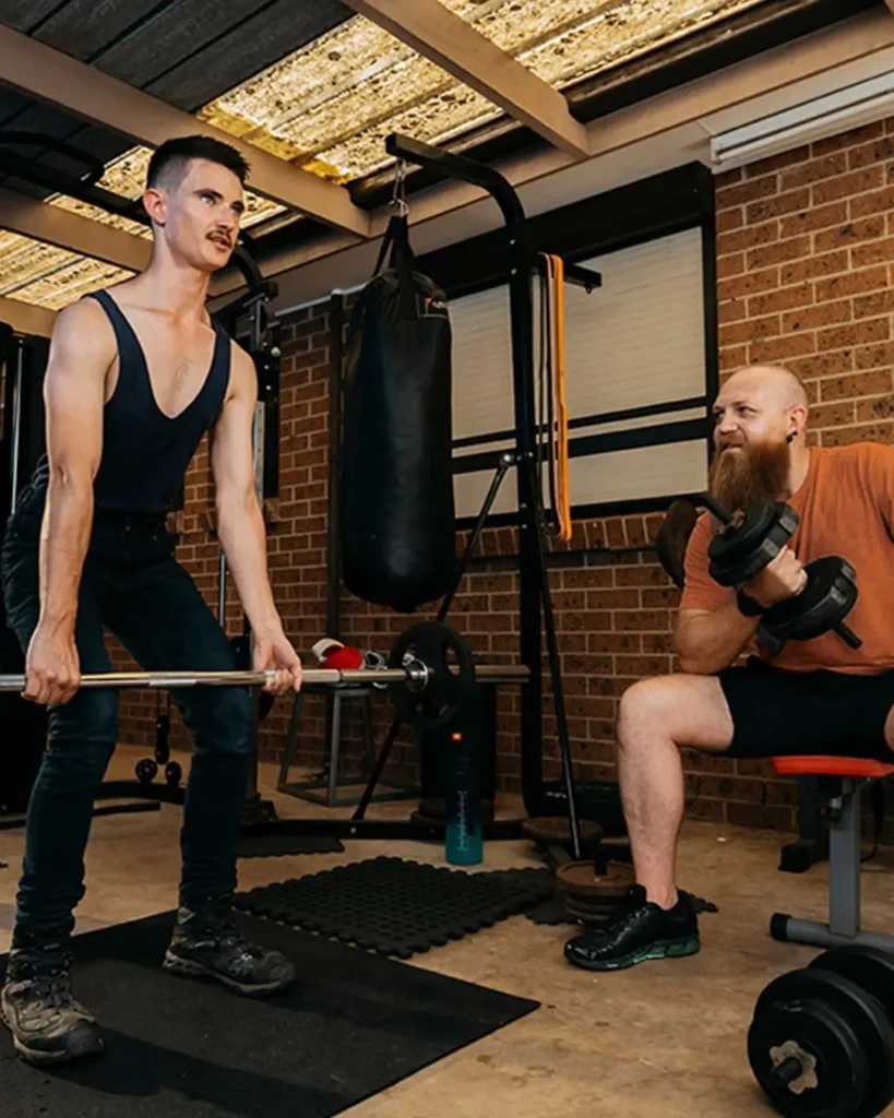 Support worker and young adult with autism and Tourette syndrome lift weights together in home gym.