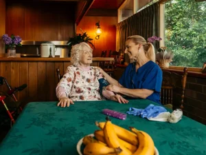 Registered Nurse takes a blood pressure reading for their older client at their dining table.