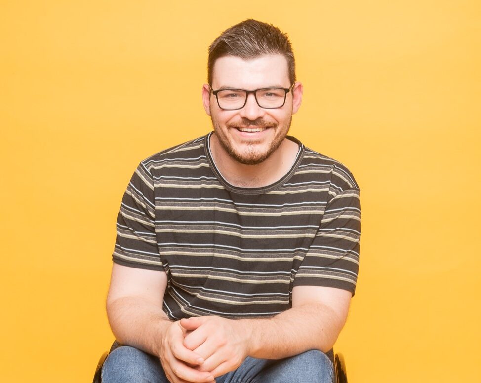 Comedian Oliver Hunter smiles against a yellow backdrop