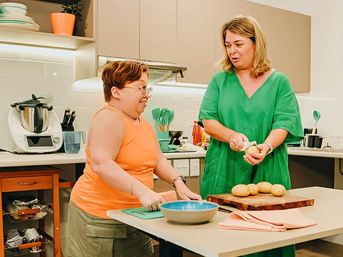 Person with disability prepares food at a low table in their accessible kitchen with support worker.