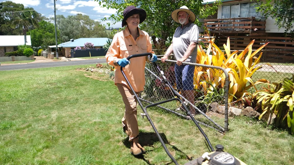 A man stands in his garden while his support worker mows the lawn.