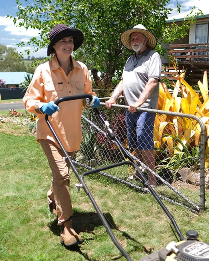 A man stands in his garden while his support worker mows the lawn.