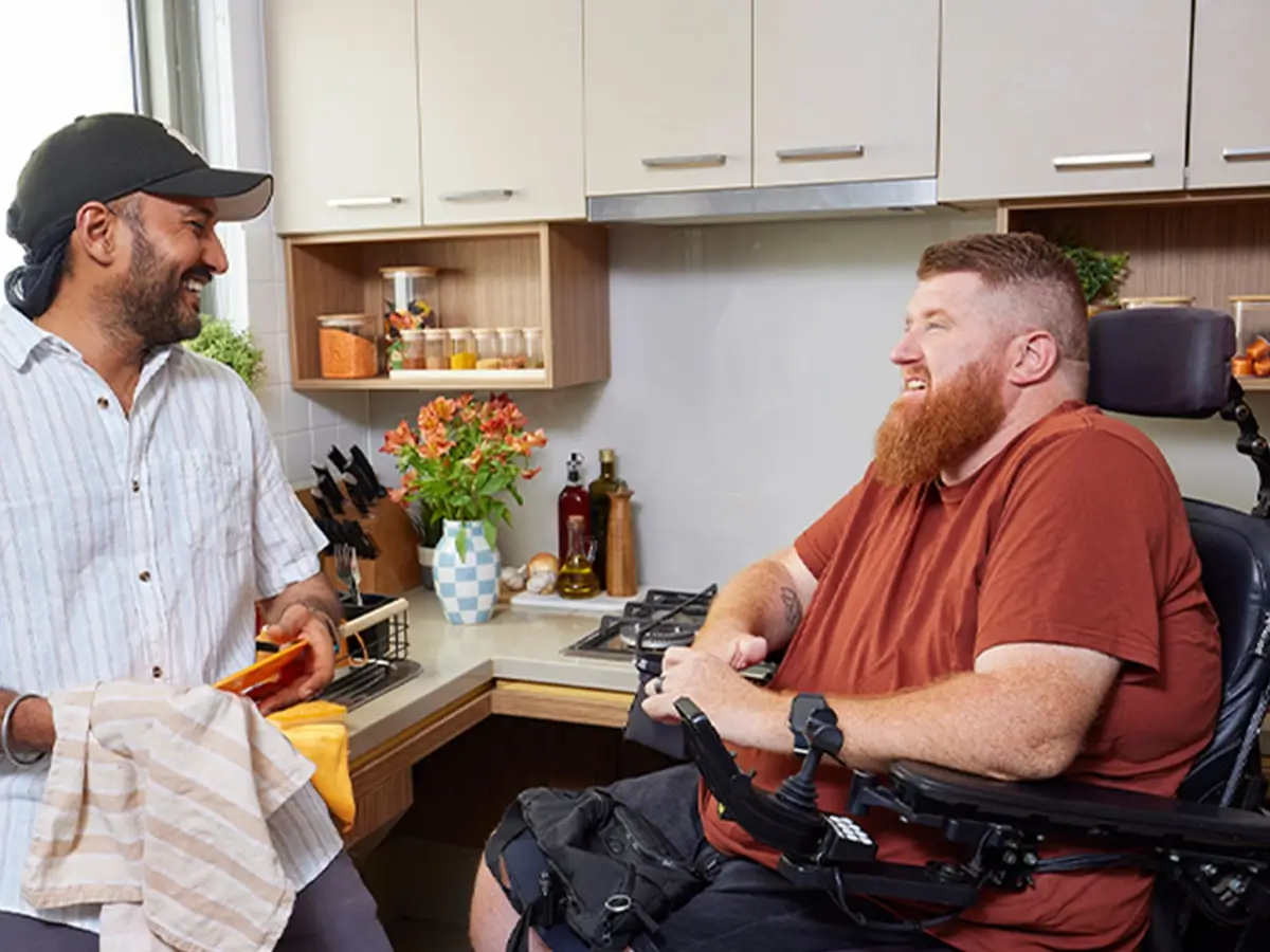 Support worker dries dishes while talking to a client who is quadriplegic and in a wheelchair.