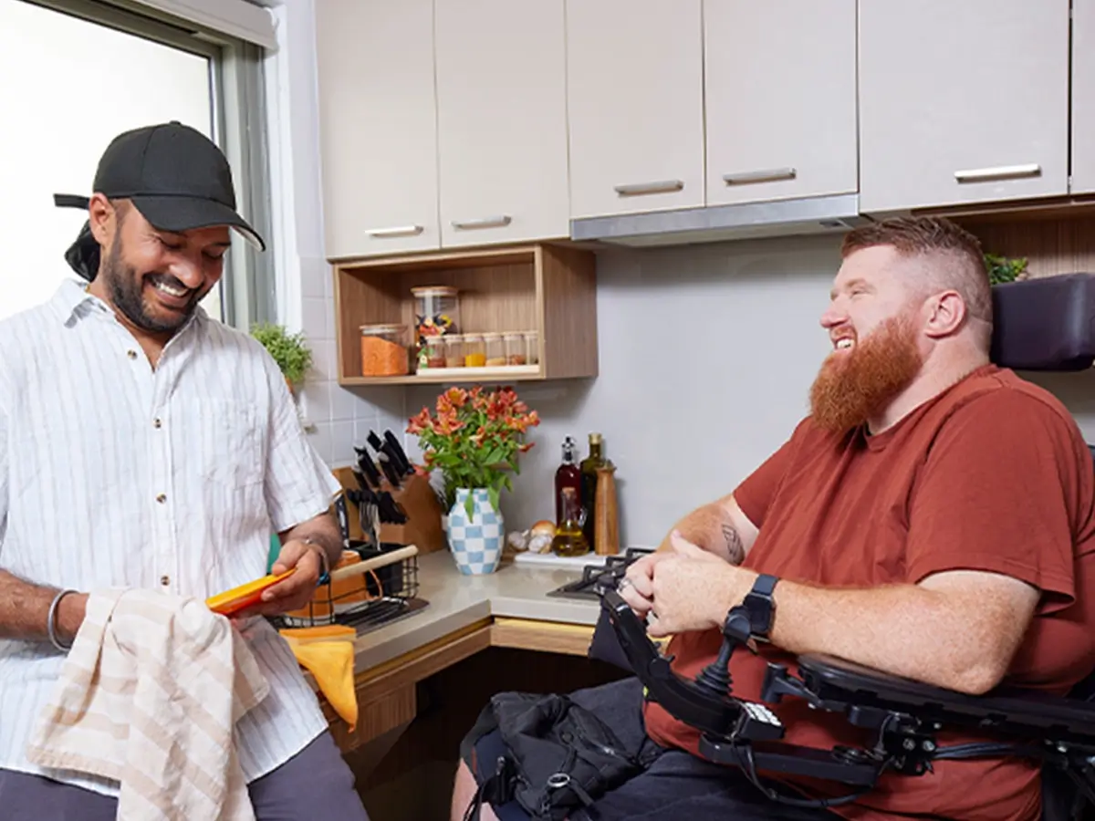 Support worker dries dishes while talking to a client who is quadriplegic and in a wheelchair.