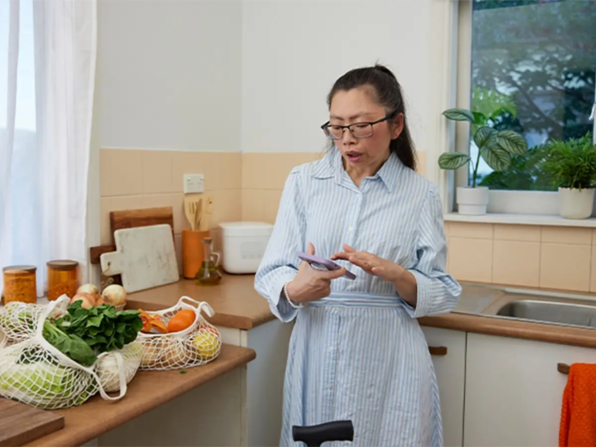 Adult with mild Cerebral Palsy standing in kitchen looking at phone.