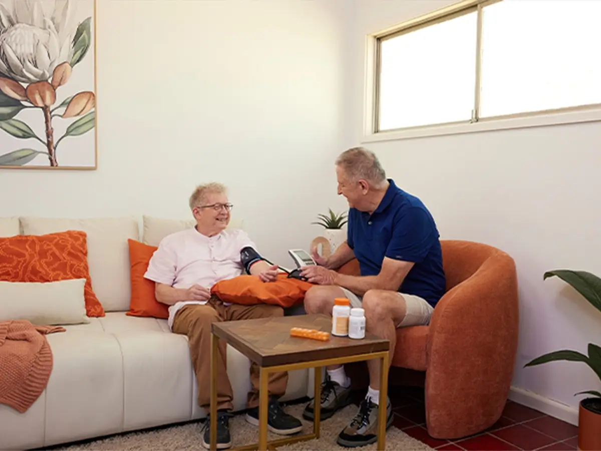 Registered nurse checking older client's blood pressure while sitting in the lounge room.