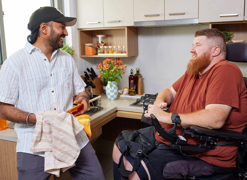 Support worker dries dishes while talking to a client who is quadriplegic and in a wheelchair.