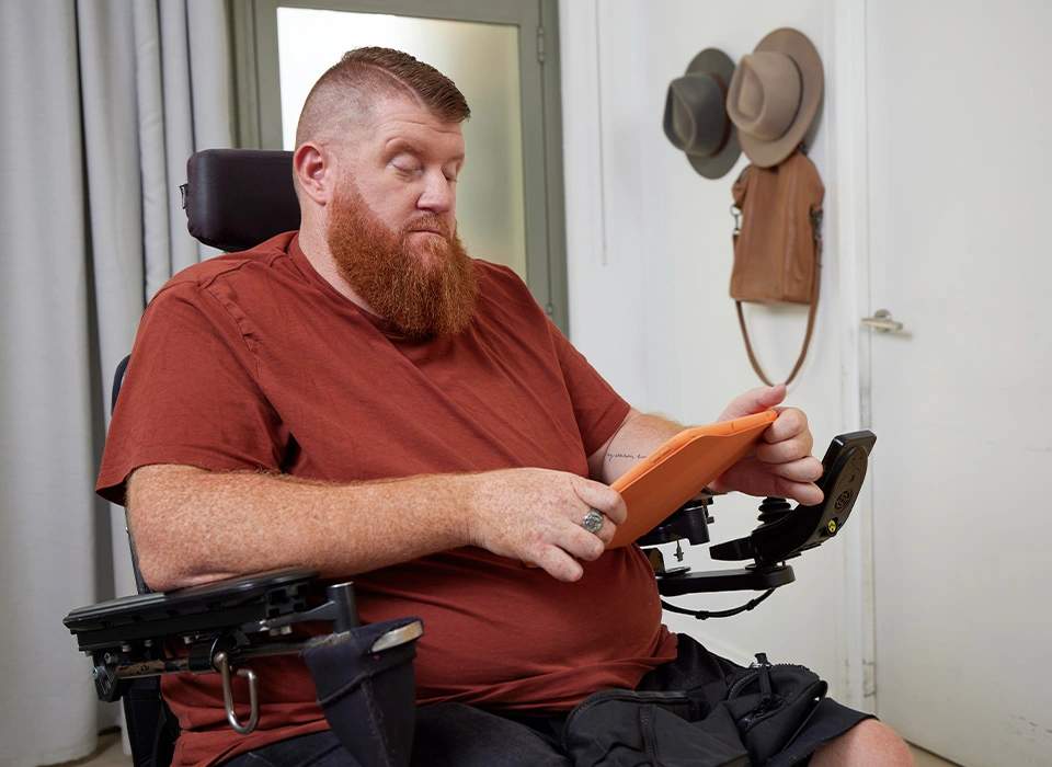 Adult who is quadriplegic and in a wheelchair looking at iPad.