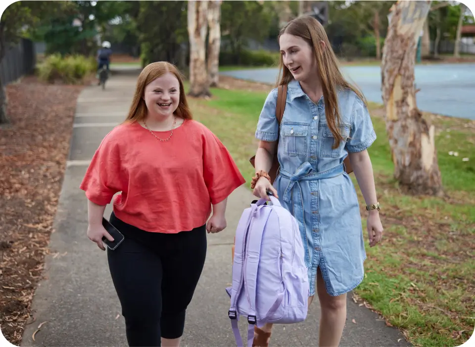 Teenager with Down syndrome walking next to support worker, who is holding a backpack.