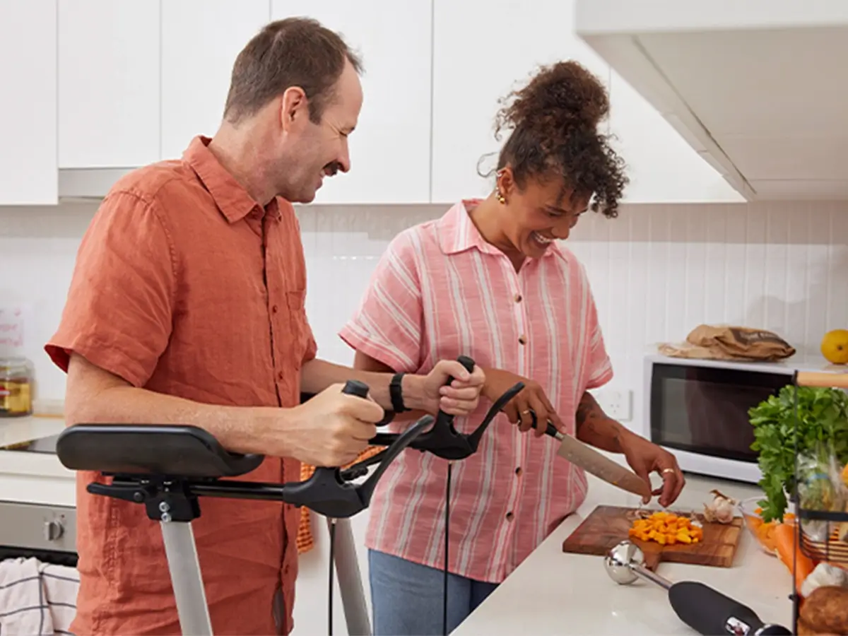 Support worker dicing pumpkin at the kitchen bench while talking to client with multiple sclerosis using a standing aid.