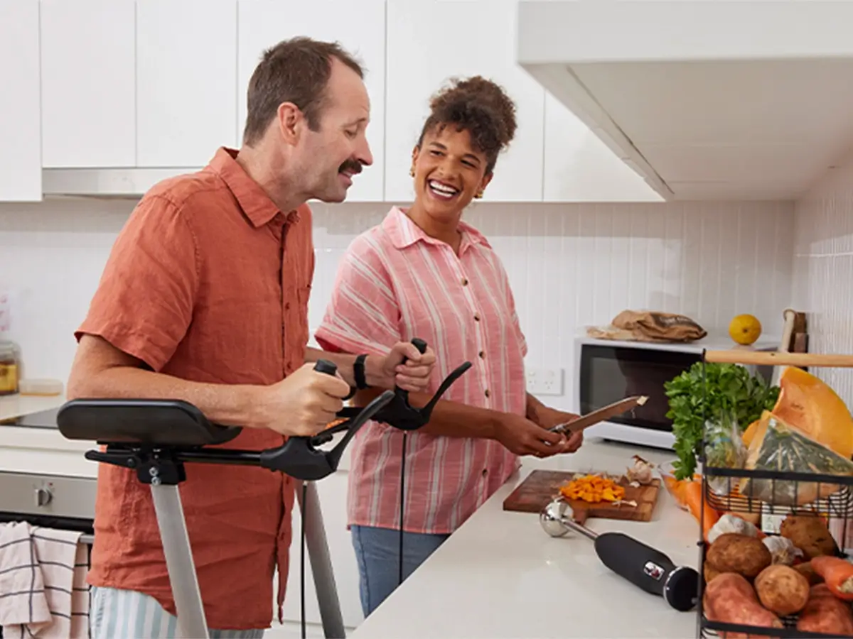 Support worker dicing pumpkin at the kitchen bench while talking to client with multiple sclerosis using a standing aid.