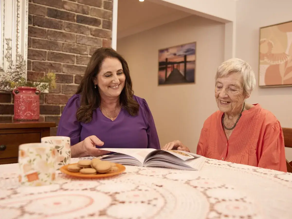 Mable client Elizabeth sits at a dining table with her independent support worker Doreen.