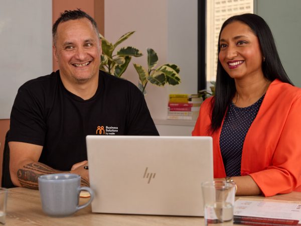 Two diverse colleagues smiling while working together at a desk with a laptop