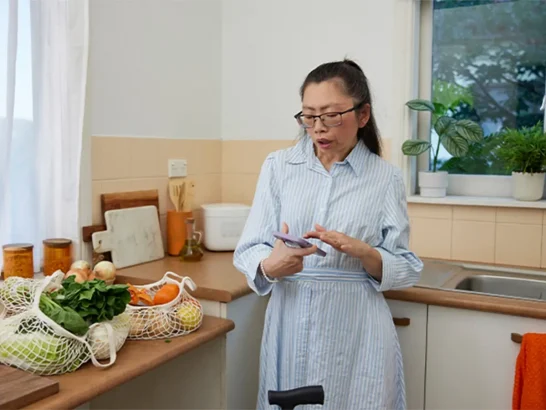 Adult with mild Cerebral Palsy standing in kitchen looking at phone.