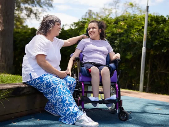 Teenager with Cerebral Palsy and in a wheelchair in a park with support worker sitting next to them.