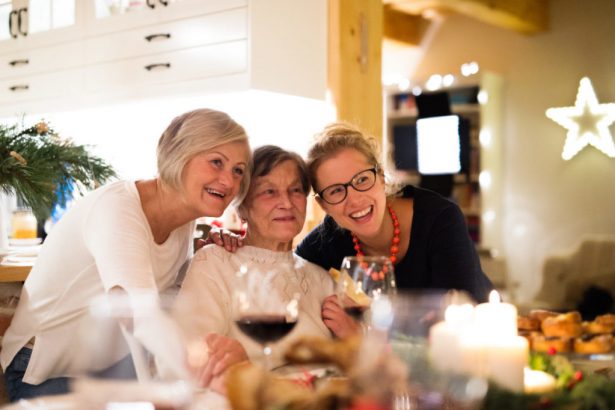 Beautiful big family sitting at the table celebrating Christmas together at home. Mother, gradmother and daughter drinking red wine.