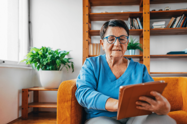 An older woman sits on the couch using her tablet.