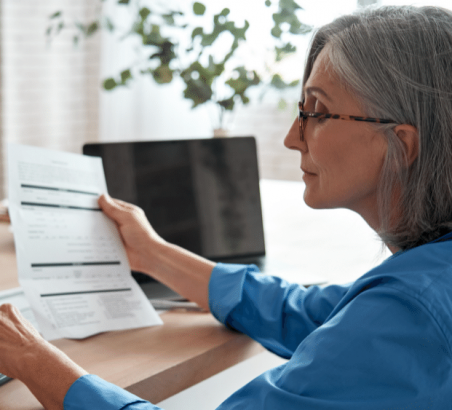 Older woman holding a document while using calculator.