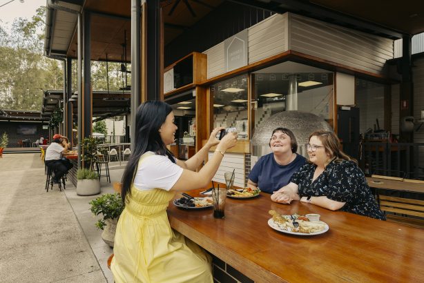 Couple with disability eating at pub pose for a photo their support worker is taking.