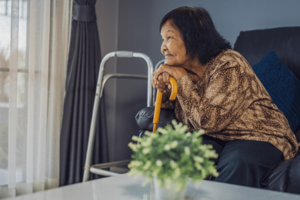 An older woman looking out a window at home.