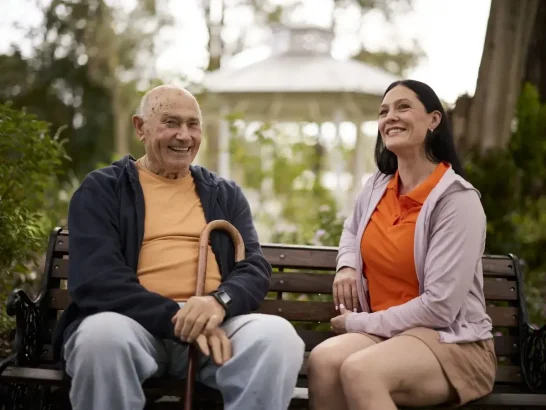 Mable client con sits on a park bench with his support worker Renee