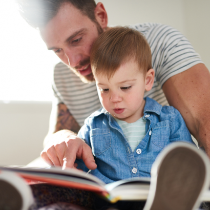 A dad and his young child reading a book together.