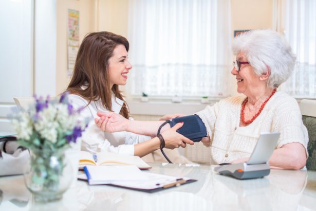 Nurse measuring blood pressure of senior woman at home.