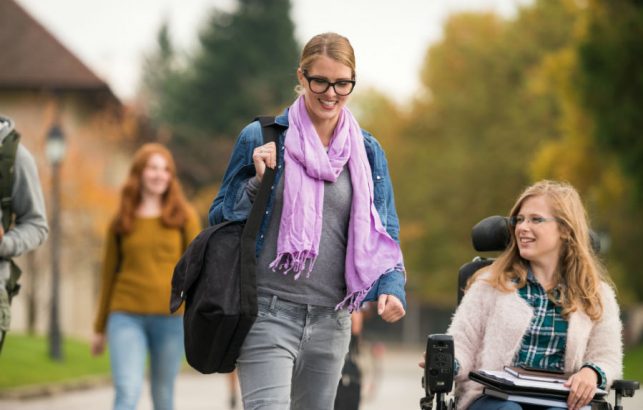 A support worker and a young woman using a wheelchair outside together.