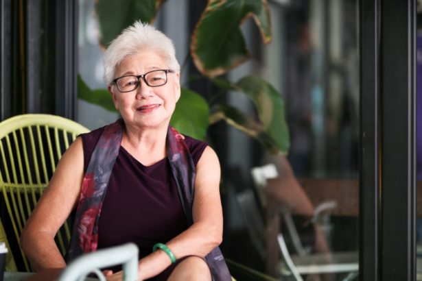 An older woman smiling while sitting outdoors.
