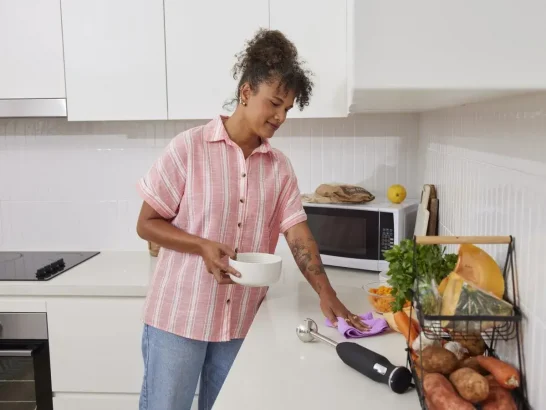 Independent support worker wipes the kitchen bench after assisting with meal prep for her client.