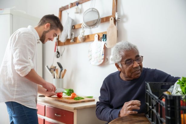 Senior person with their support worker helping chop vegetables in the background