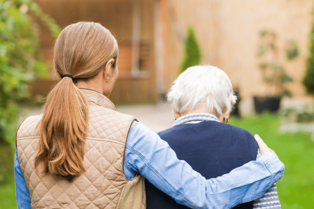 An older woman walking outdoors with her support worker.