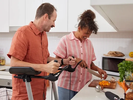Support worker dicing pumpkin at the kitchen bench while talking to client with multiple sclerosis using a standing aid.