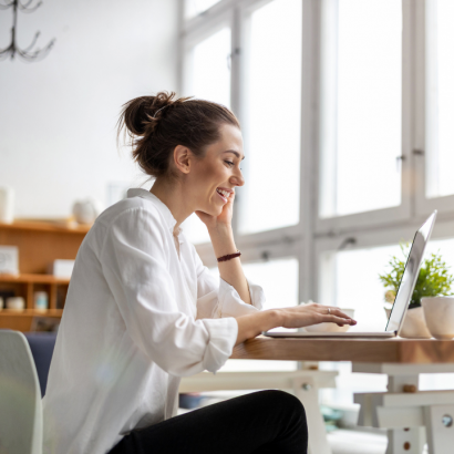 woman in bright home office environment smiling while working on laptop