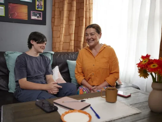 Teenage Mable client Wyatt sits on the couch talking with his independent support worker